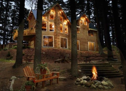 exterior shot of Katahdin Cedar Log Home at night with chairs and fire pit in foreground